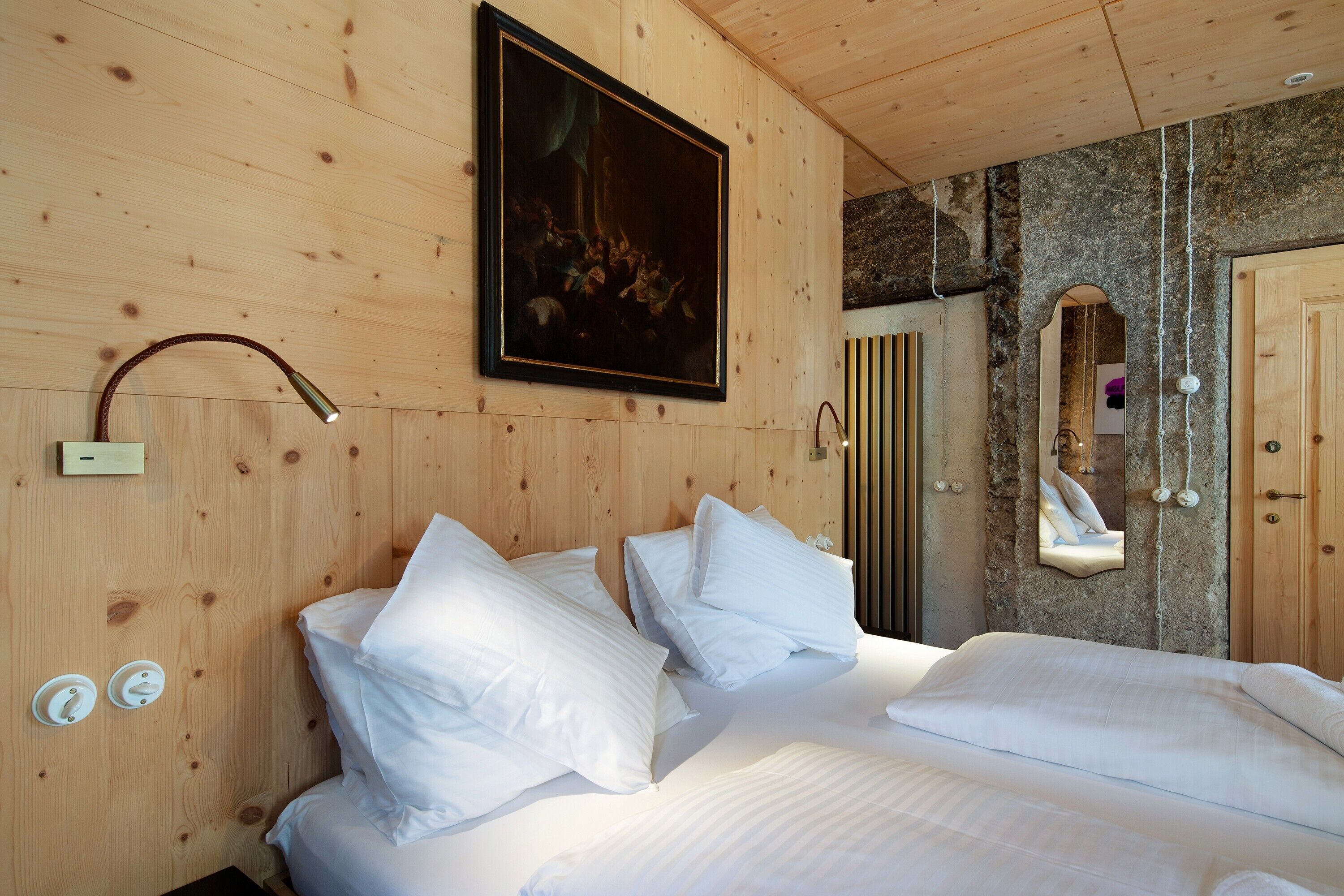 Une pièce aux murs lambrés, avec un lit, un tableau, un miroir et un mur en pierre.