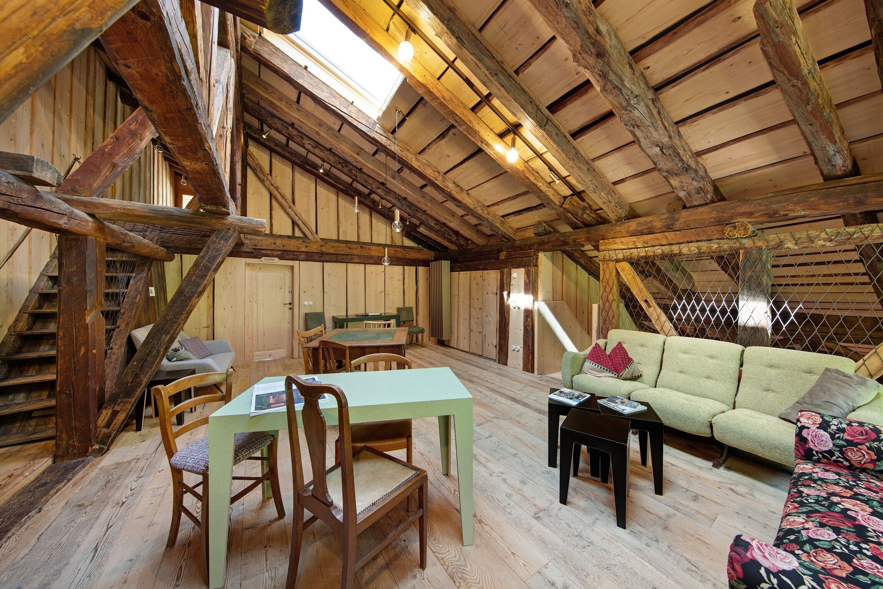 Un interior rústico de madera con una mesa de comedor, sillas, un sofá y una escalera.