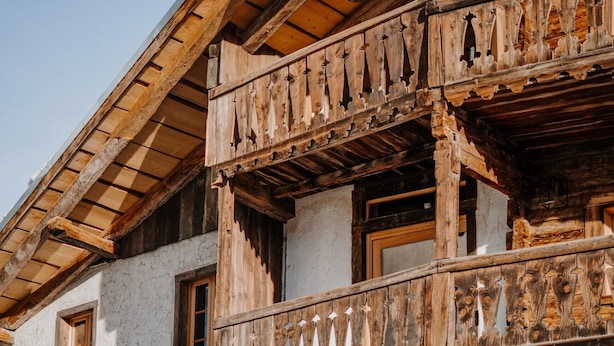 Een landelijk gebouw met een houten balkon, een grote houten deur en meerdere ramen.