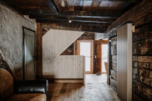 A rustic wooden interior with a sloped ceiling, a wooden bench, a door, and a view through an open doorway.