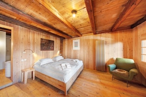 Ein Zimmer mit Holzwänden, einem Bett, einem Sessel und einem kleinen Tisch.