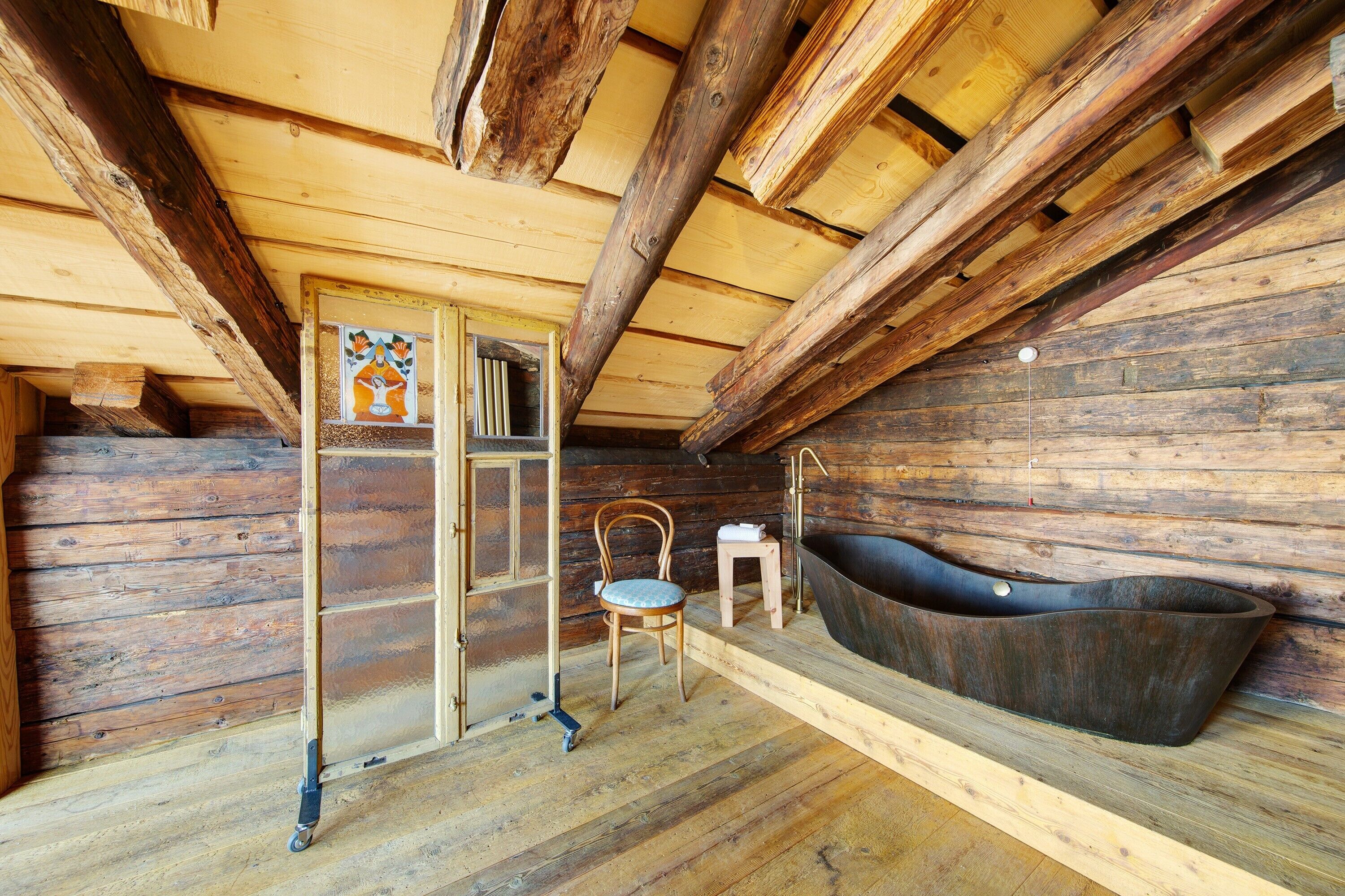 A rustic wooden cabin interior with a wooden floor, a large bathtub, a wooden chair, and a small table.