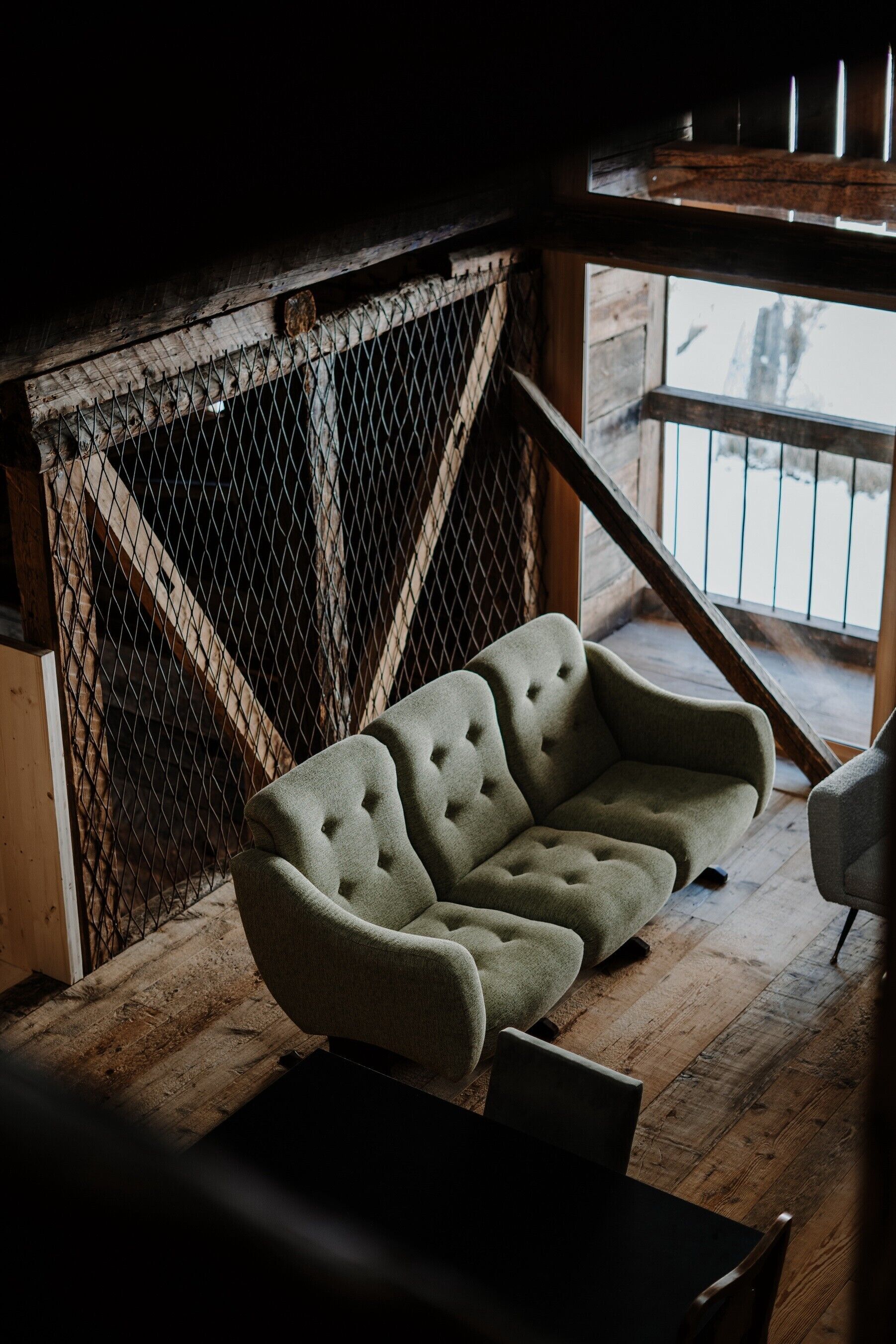 Ein gemütliches Zimmer mit einem grünen gepolsterten Sofa, Holzboden und einem Metallzaun.
