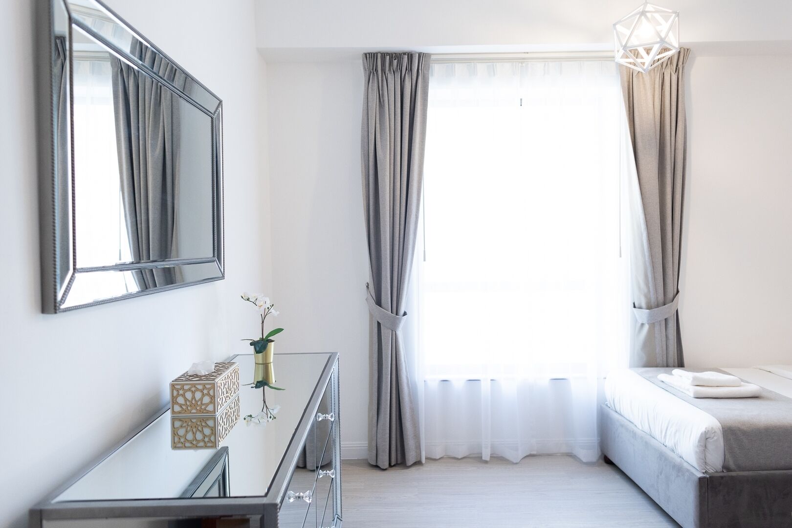A bedroom with a bed, a dresser, a mirror, and a window with curtains.