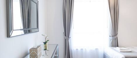 A bedroom with a bed, a dresser, a mirror, and a window with curtains.