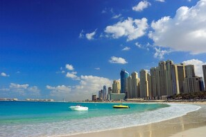 A beach with clear turquoise waters, a sandy shore, and a city skyline with high-rise buildings in the background.