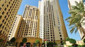 A high-rise building with multiple floors, a central entrance, and surrounding greenery. - 2BR apartment Sea View Upgraded on JBR (Dubai)