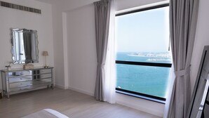 A hotel room with a large window, a dresser, a mirror, and a view of the sea. - 2BR apartment Sea View Upgraded on JBR (Dubai)