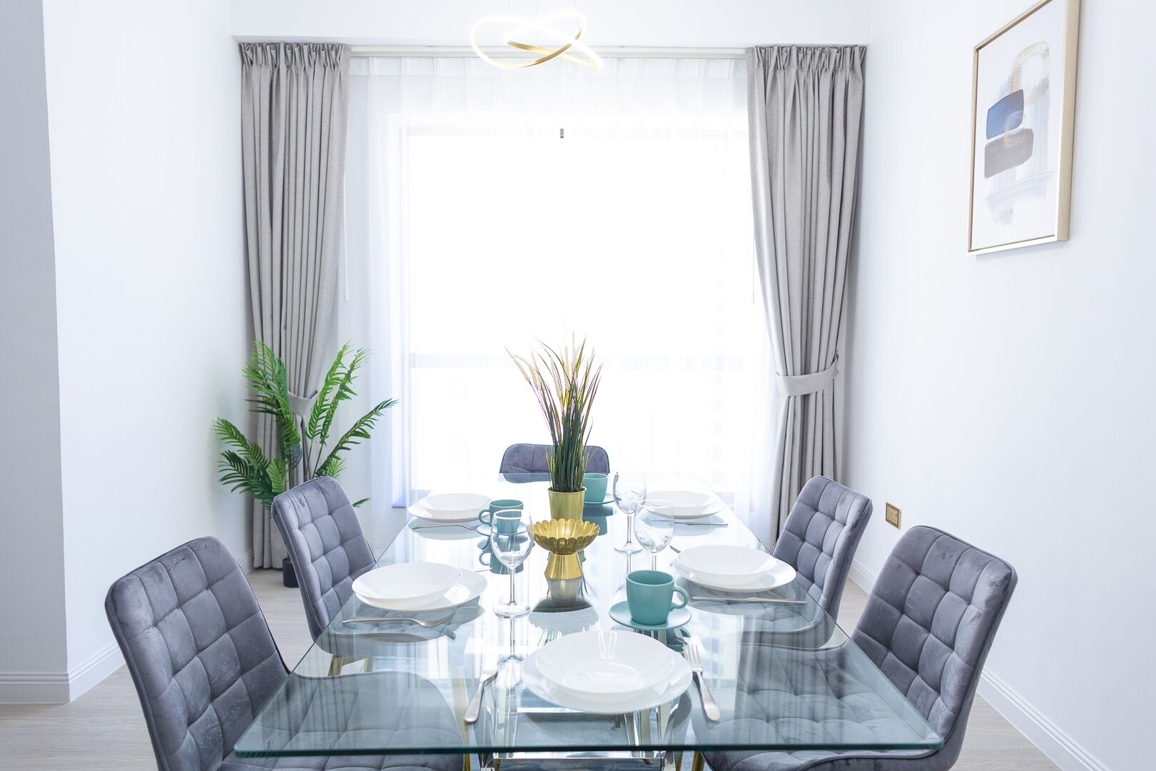 A dining area with a glass table, grey upholstered chairs, and a vase with plants.