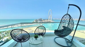 Een balkon met twee stoelen en een hangstoel met uitzicht op een strand en een brug.