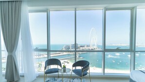Een kamer met een groot raam met uitzicht op een jachthaven en een reuzenrad, met twee stoelen en een klein tafeltje.