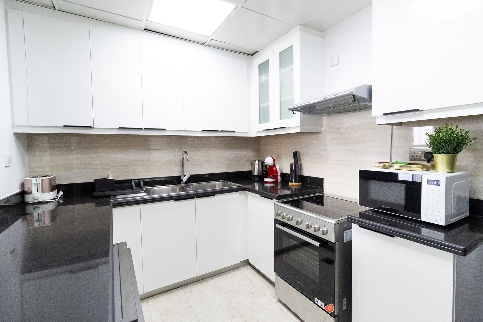 A modern kitchen with white cabinets, a black countertop, a stainless steel sink, a gas stove, an oven, and a microwave.