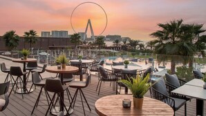 Un bar en la azotea con mesas al aire libre y vistas a una noria al atardecer.