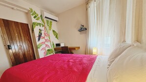 A hotel room with a bed, a desk with a chair, an air conditioning unit, and a wall-mounted lamp. - Heliconia Room Eden On The Sea Carlisle Bay Barbados  (Bridgetown)