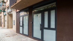 Une façade d’immeuble avec des portes numérotées, un trottoir carrelé et une enseigne de pharmacie bien visible.