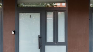 Une entrée d’immeuble avec une grande porte vitrée, le chiffre « 5 » sur la porte et une petite boîte aux lettres fixée au mur.