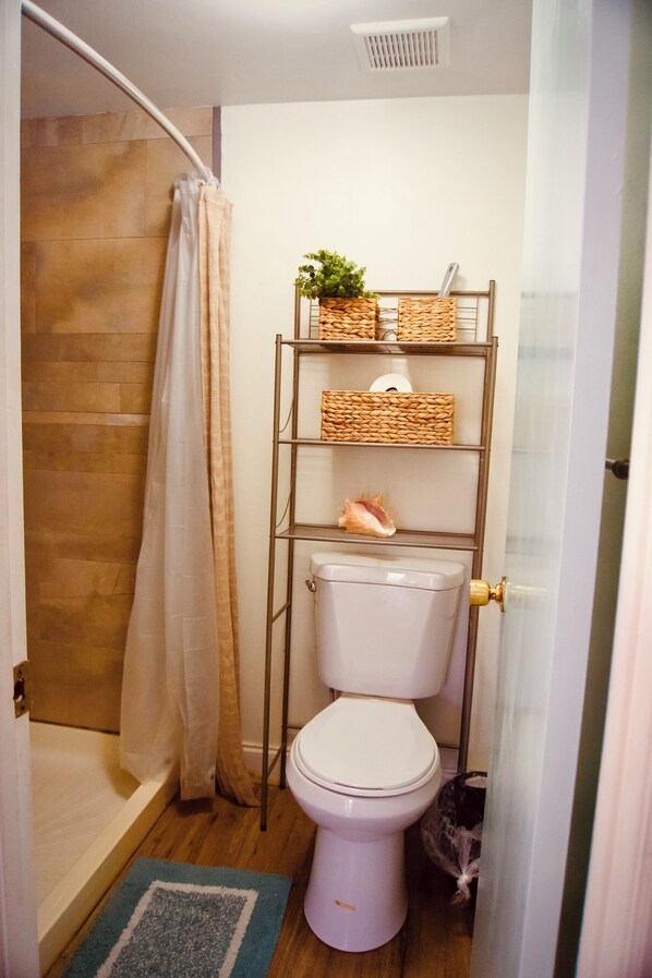 Un baño con ducha, inodoro y estante con cestas.