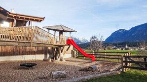 Eine Holzterrasse mit einer roten Rutsche, einem Holzzaun und einem Berg im Hintergrund.