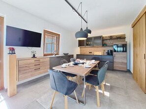 A modern kitchen with a dining area, wooden cabinets, and a flat-screen TV.
