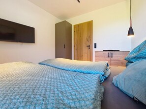 A bedroom with two beds, a wooden wardrobe, a TV mounted on the wall, and a hanging light fixture.