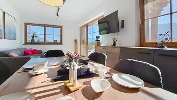Een eethoek met een tafel voor vier personen, een flatscreen televisie aan de muur en een raam met uitzicht op bergen.