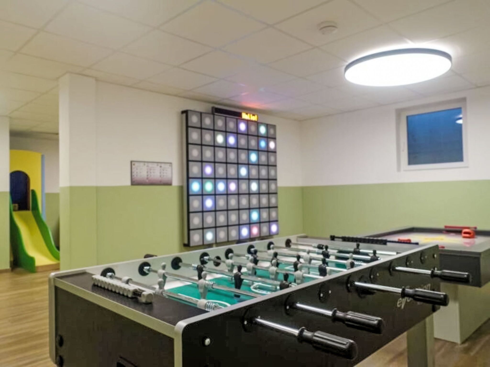 Een kamer met een tafelvoetbaltafel, een kleurrijk paneel met LED-verlichting en een glijbaan.