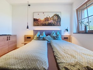 A bedroom with two beds, a nightstand, a dresser, a painting, and a window with a plant.