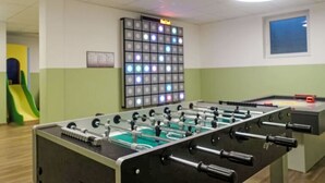 Huone, jossa on pöytäjalkapallopeli, värikäs LED-valopaneeli ja liukumäki.