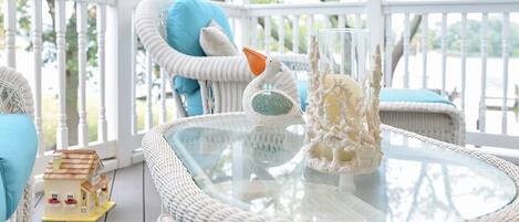 A wicker outdoor seating area with a glass table, a small house model, and decorative items.