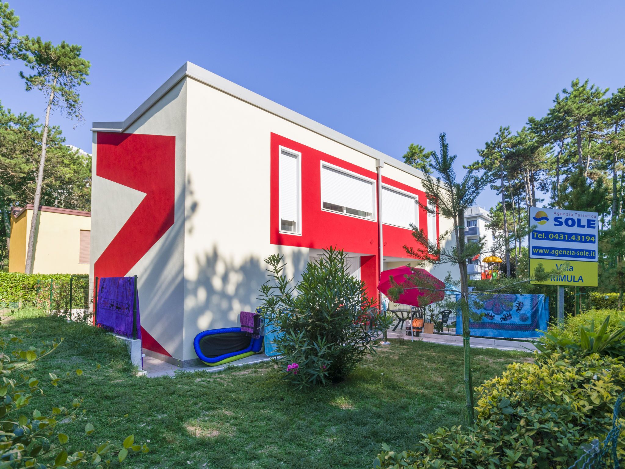 Een modern gebouw met een rood-witte gevel, een kleine tuin met een blauwe speelconstructie, en een bord waarop een toeristenbureau wordt aangekondigd.