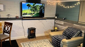Un salon chaleureux avec un téléviseur, un petit poêle à bois, un canapé confortable et un tapis à motifs.