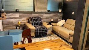 Un salon chaleureux avec une table à manger en bois, un canapé et un fauteuil. On peut voir un globe sur la table et une horloge au mur.