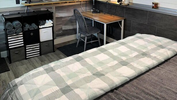 Une petite pièce comprenant un lit, un bureau avec un ordinateur, une chaise et un téléviseur.