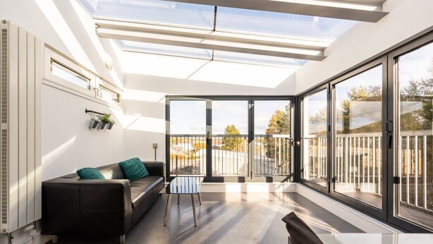 A modern living room with a glass ceiling, a black leather sofa, a small table, and a view of the outside. - GuestReady - Spacious 2Bed in Edinburgh (Edinburgh)