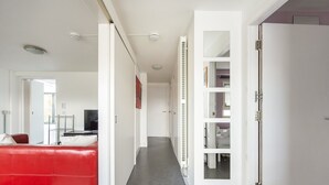 A modern interior with a red sofa, white walls, and a hallway leading to a room with a bed and a TV. - GuestReady - Spacious 2Bed in Edinburgh (Edinburgh)