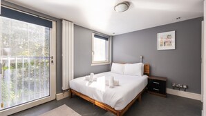 A bedroom with a large sliding glass door, a bed with white linens, a nightstand, and a wall-mounted power outlet. - GuestReady - Spacious 2Bed in Edinburgh (Edinburgh)