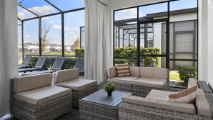 Un área de estar al aire libre con luz solar, muebles de mimbre y vistas del barrio.