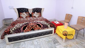 A bedroom with a bed, a nightstand, a chair, and a small table with a candle. - The Desert Dhani Resort (Jaisalmer)