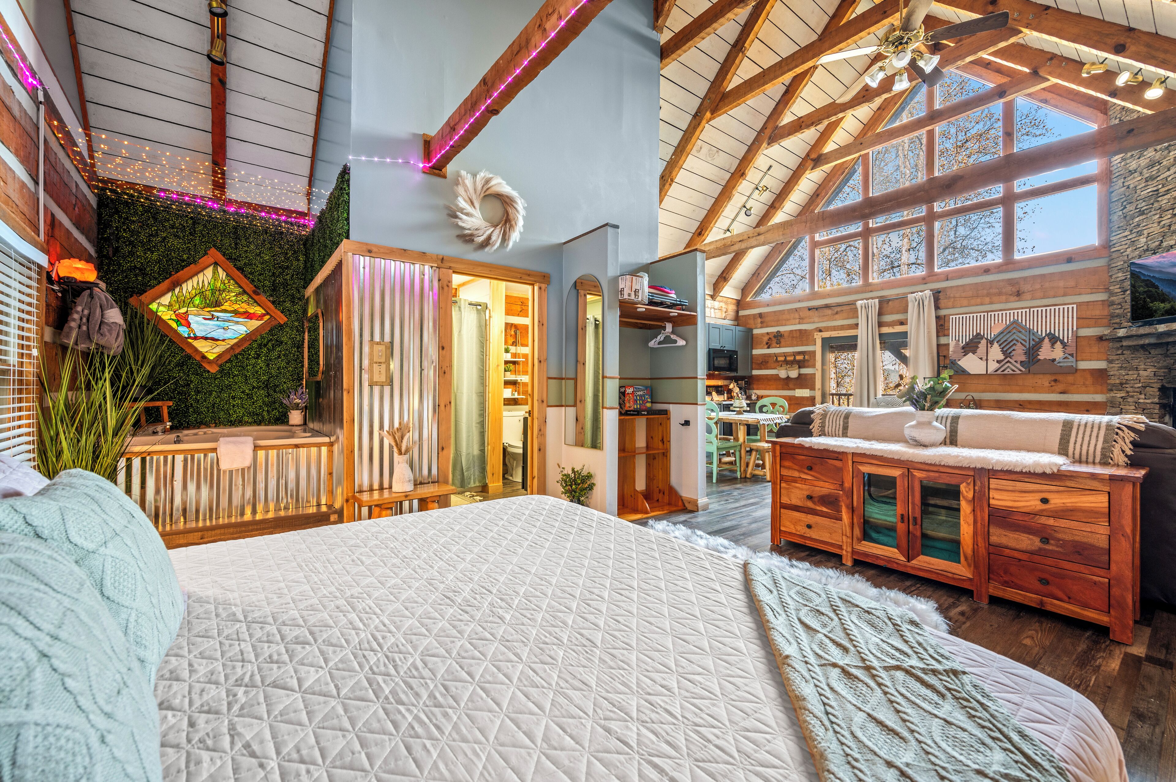Een ruime slaapkamer met een groot bed, houten balken in het plafond en uitzicht op de keuken en eetruimte.