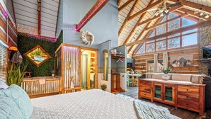 Un dormitorio amplio con una cama grande, vigas de madera en el techo y vistas al área de la cocina y el comedor.