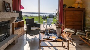 Ein gemütliches Wohnzimmer mit Kamin, bequemen Sitzgelegenheiten, einem Couchtisch und Meerblick.