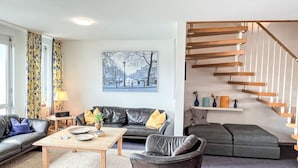 A modern living room with a black leather sofa, a wooden coffee table, and a staircase with wooden railings. - Schwarzwaldblick VI by Interhome (Bernau)