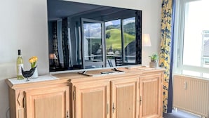 A wooden cabinet with a large mirror above it, a bottle of wine, and a vase with flowers on a small table. - Schwarzwaldblick VI by Interhome (Bernau)