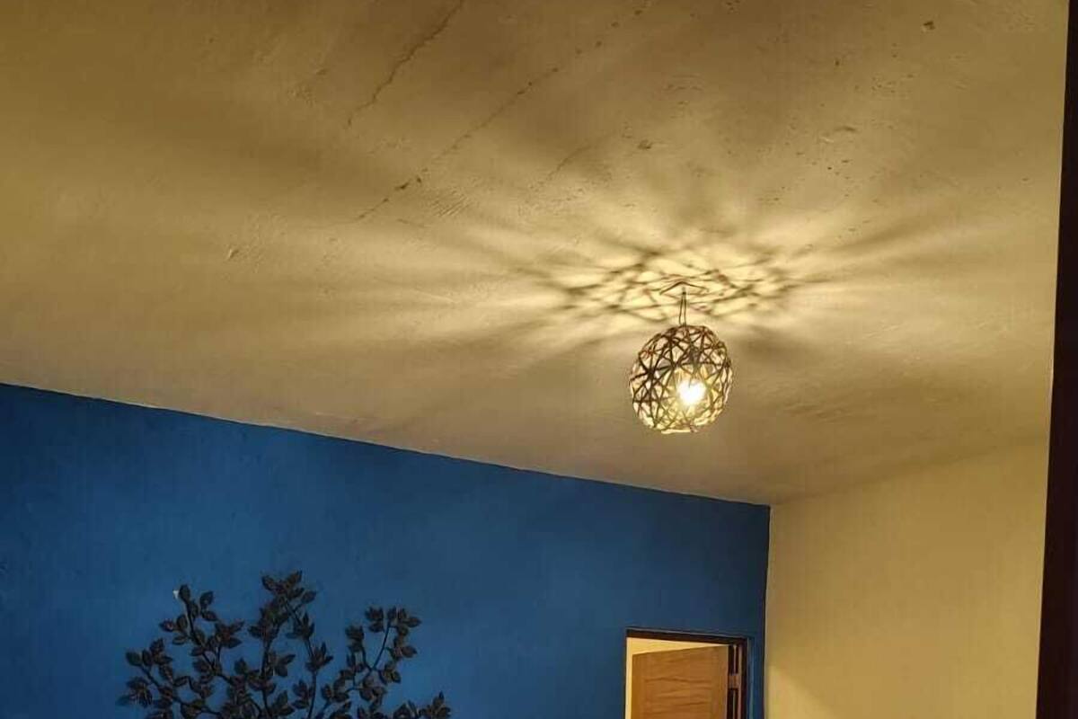 Egy hálószoba, amelyben van egy ágy, egy falfestmény, egy ajtó és egy mennyezeti lámpatest.