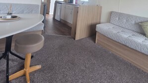 A compact living space with a kitchenette, a dining area with a table and bench, and a sofa. - Steve caravan Sleeps 6 with Free Parking (Rhyl)