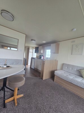 A compact living space with a kitchenette, a dining area with a table and bench, and a sofa.