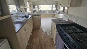 A compact kitchen with a gas stove, a sink, and a dining area with a table and chairs. - Ruby Cabin Sleeps 6 with Free Parking (Rhyl)