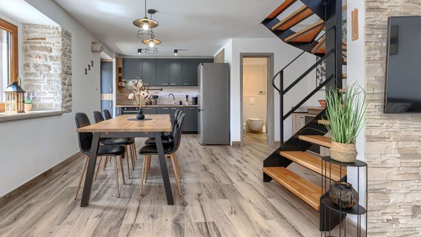 Une cuisine moderne avec des meubles de couleur sombre, une table à manger en bois et un escalier au design original.