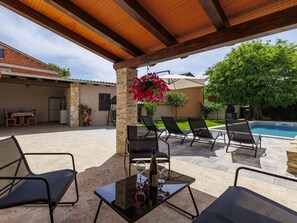 An outdoor patio with a pool, stone walls, and a wooden pergola.