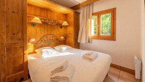 A wooden-paneled bedroom with a bed, two wall-mounted lamps, a window with curtains, and a radiator. - Le Cristal GM9 Mountain View, Pool, Parking & Free WiFi, Argentière (Chamonix), France (Argentière (Chamonix))